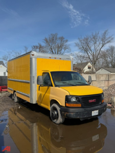 GMC Savana box truck in yellow with a large cargo box and cab, front view, parked on wet ground.