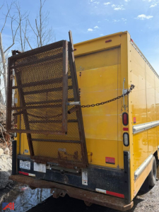GMC Savana box truck rear view showing yellow cargo box with ramp gate and chained rear door, black bumper, tail lights, and license plate area.