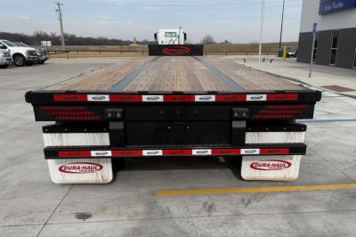 Rear view of a flatbed trailer with wooden deck and white mud flaps showing DURA-HAUL branding and reflective stripes.