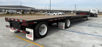 Drop deck trailer showing long flatbed with dual rear axles and white fenders.