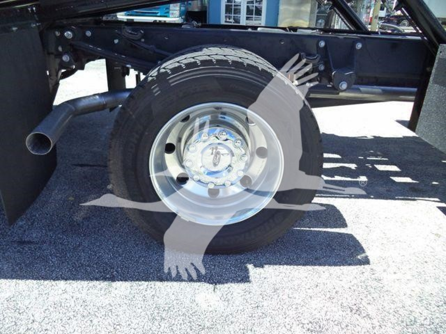Wheel and tire of new Ford F600 rollback truck chassis showing steel rim and tire with frame and exhaust nearby.