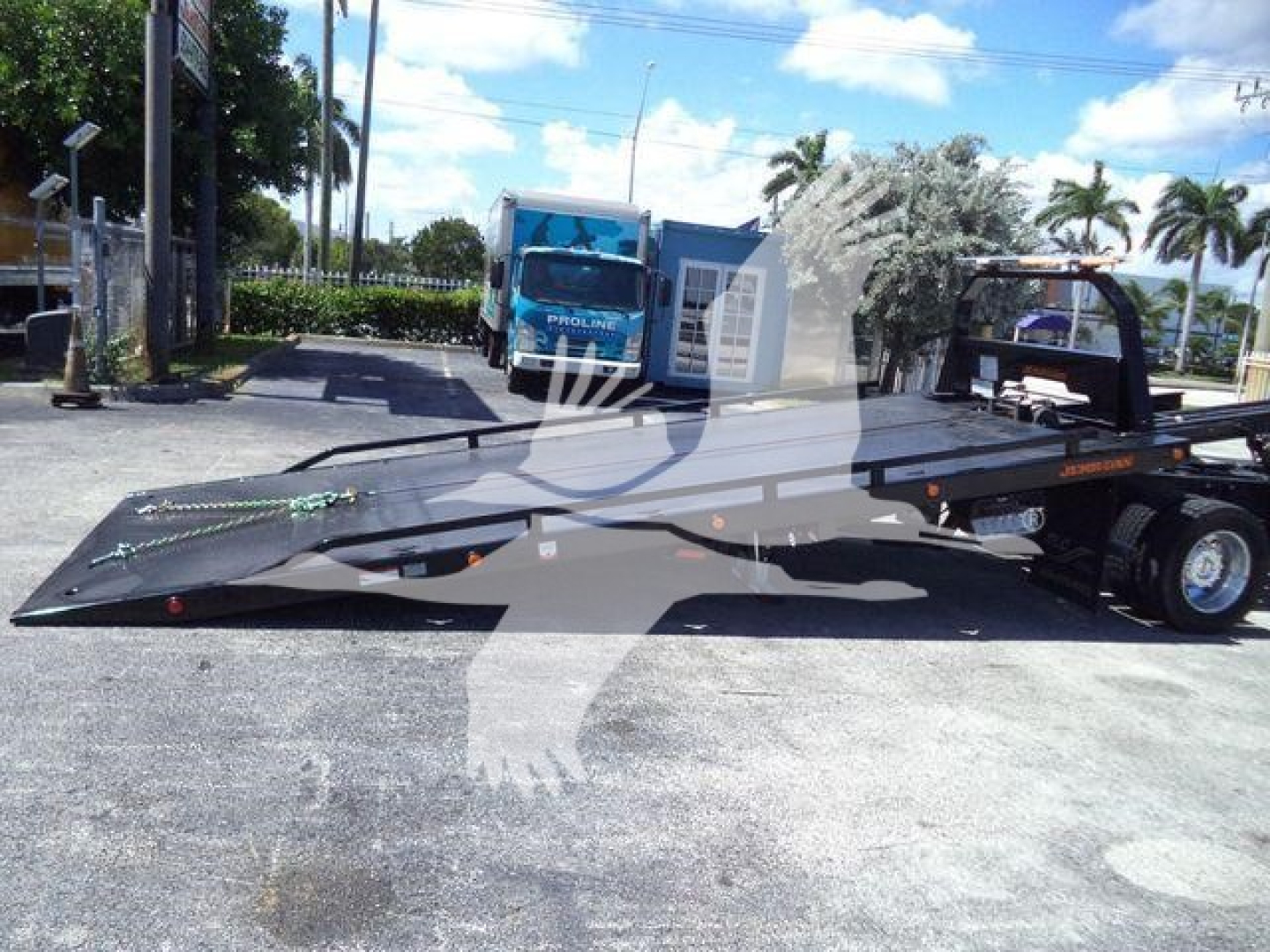 Ford F-600 flatbed rollback tow truck with a long ramp platform in a parking lot.