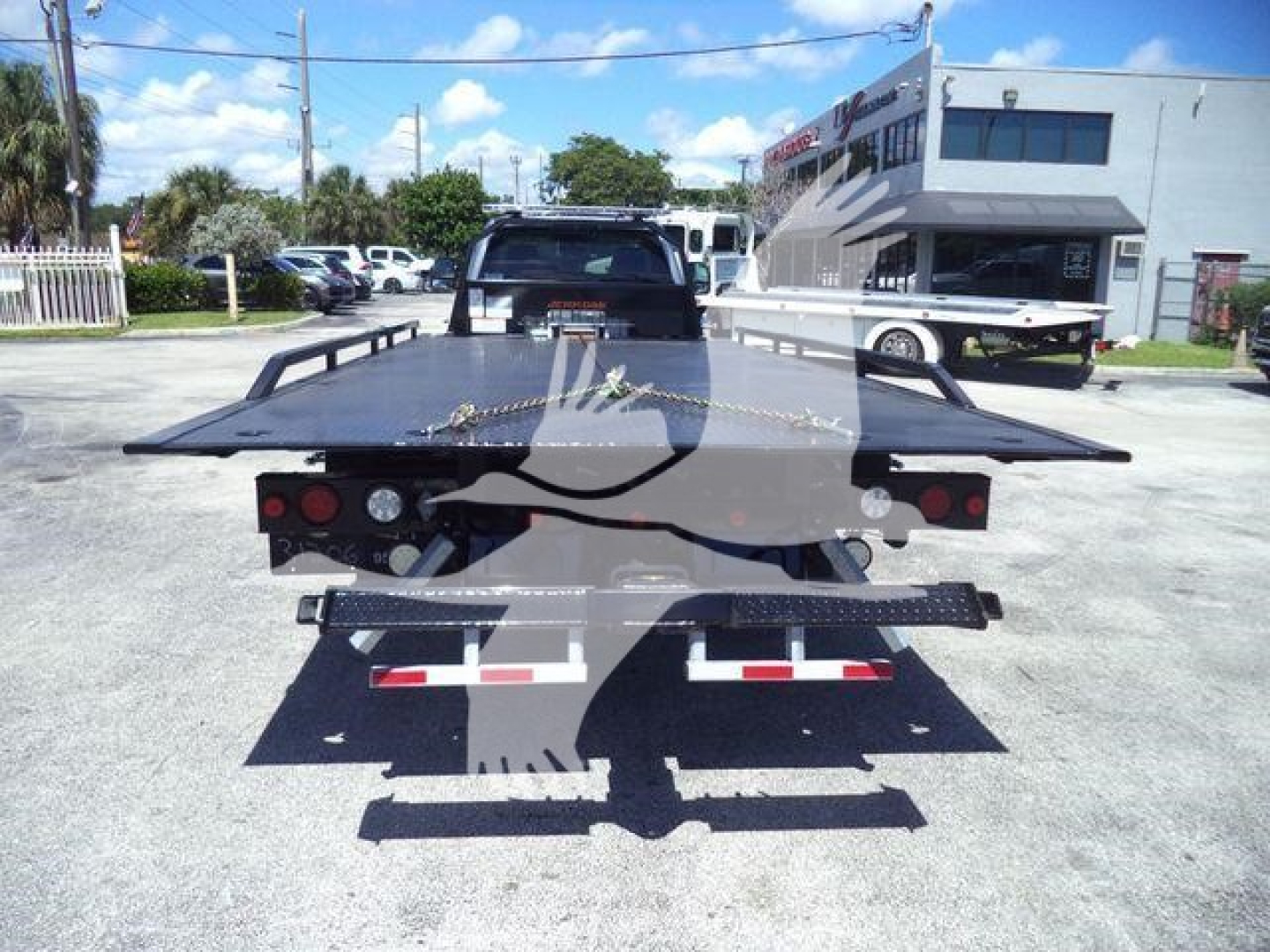 Rear view of a 2024 Ford F-600 rollback tow truck with a flatbed, rear lights, and towing equipment visible.