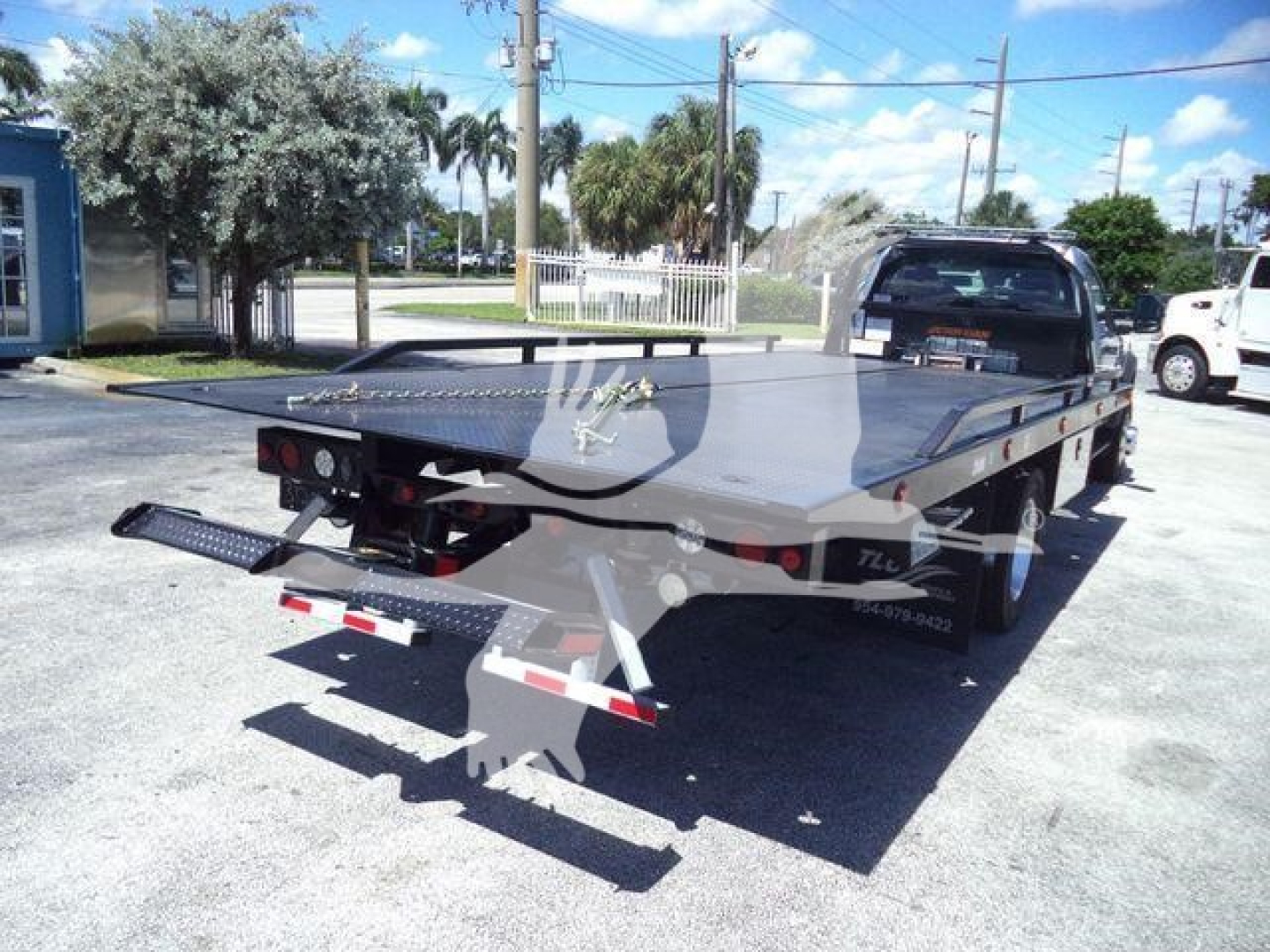 Flatbed rollback tow truck with a steel deck and rear ramps, F600 XLT branding not visible, showing dual rear wheels and a mounted gooseneck hitch.