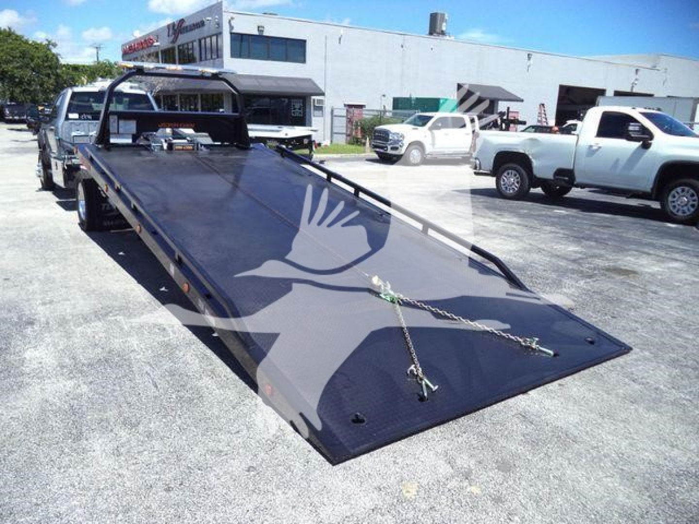 Flatbed tow truck bed on a new Ford F600 XLT with metal ramps and wheel chocks in a dealership lot.