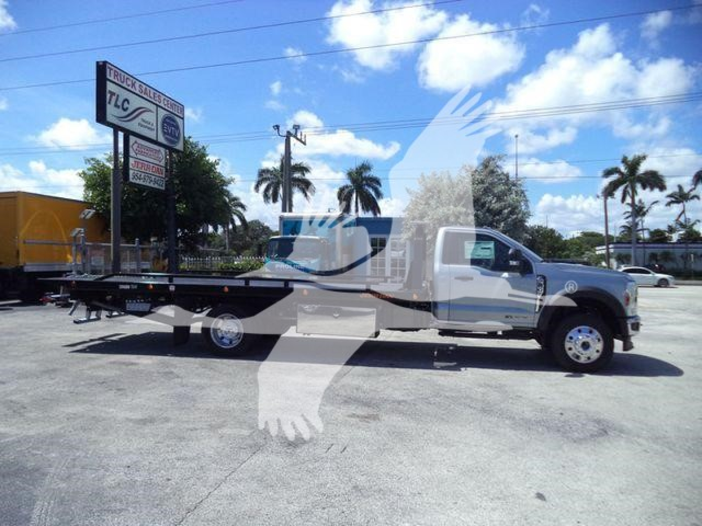 Ford F-Series flatbed rollback truck in service bay with sign in background showing dealership branding.