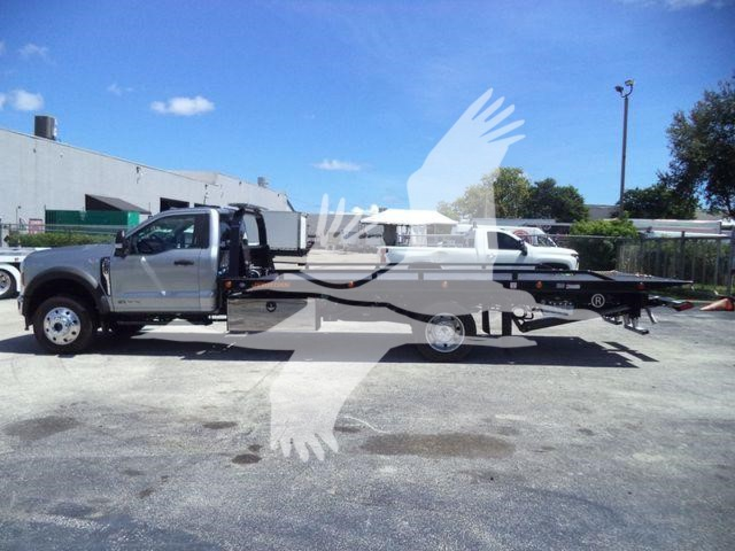 Truck in a parking lot showing a 2024 Ford F600 XLT rollback tow truck with extended flatbed and tow setup visible.