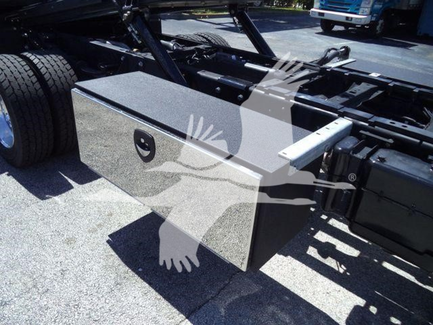 Truck chassis with a rectangular storage toolbox mounted near the frame rail and dual rear wheels visible.