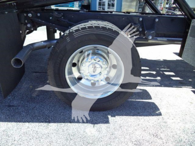 Wheel and tire of new Ford F600 rollback truck chassis showing steel rim and tire with frame and exhaust nearby.