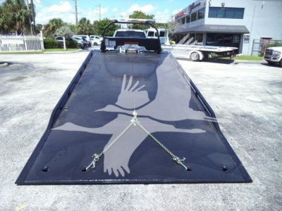 Ford F-Series rollback truck bed in view with ramp lowered, showing tie-down straps and chain anchors on glossy black surface