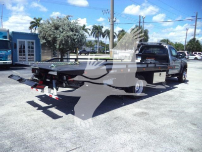 Flatbed rollback tow truck with a Ford F-600 XLT truck cab behind a flatbed; visible equipment includes a long flatbed, towing winch, rear ramps, and side rails.