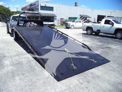 Flatbed tow truck bed on a new Ford F600 XLT with metal ramps and wheel chocks in a dealership lot.