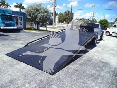 Truck bed with a lowered flatbed/roll-off style on a Ford F-600 XLT chassis, showing the front cabin area and ramp surface in a dealership lot.