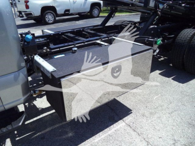 Truck chassis with aluminum toolbox mounted behind cab; flatbed rollback equipment visible; toolbox lid with handles and latches; Ford F-Series truck frame in background