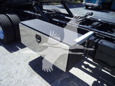 Truck chassis with a rectangular storage toolbox mounted near the frame rail and dual rear wheels visible.