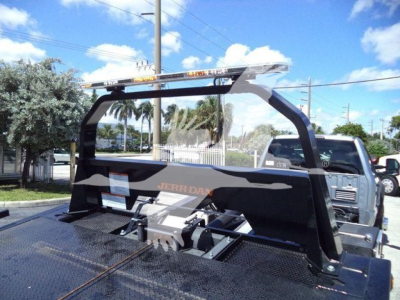 Front view of a rollback tow truck with a heavy-duty steel frame and a mounted winch, JERR-DYNE logo on side, and a light bar on top of the cab; blue sky with palm trees in background.