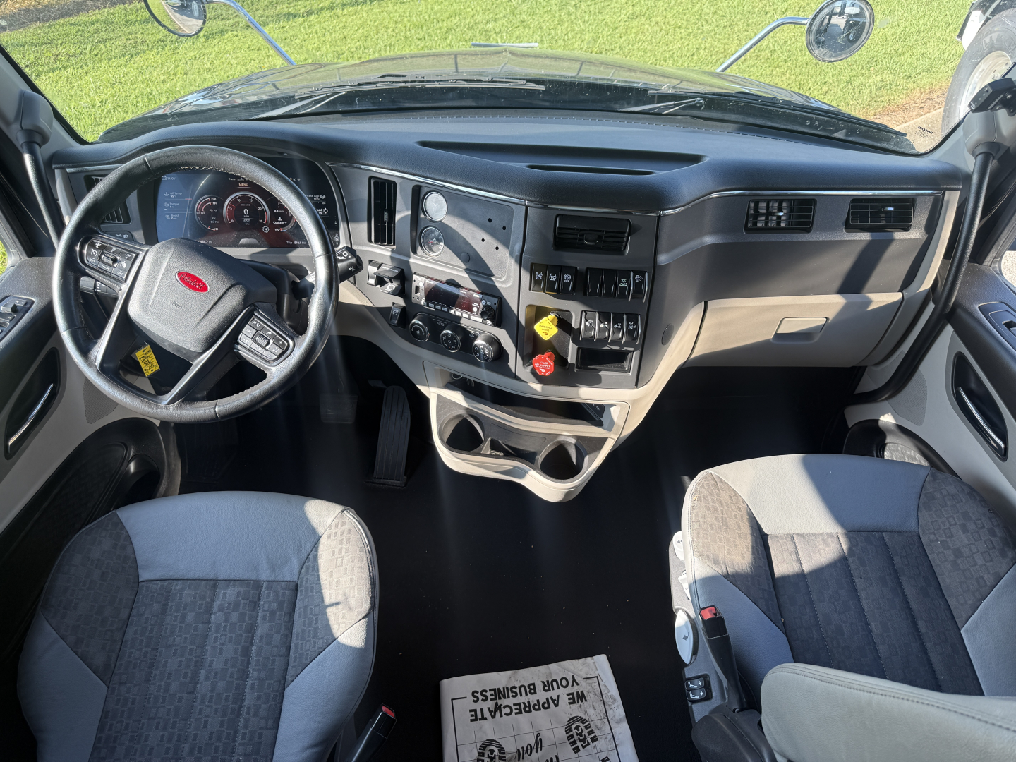 Peterbilt 579 cab interior showing steering wheel and dashboard with gauges, center console, gear shifter, and two seats.