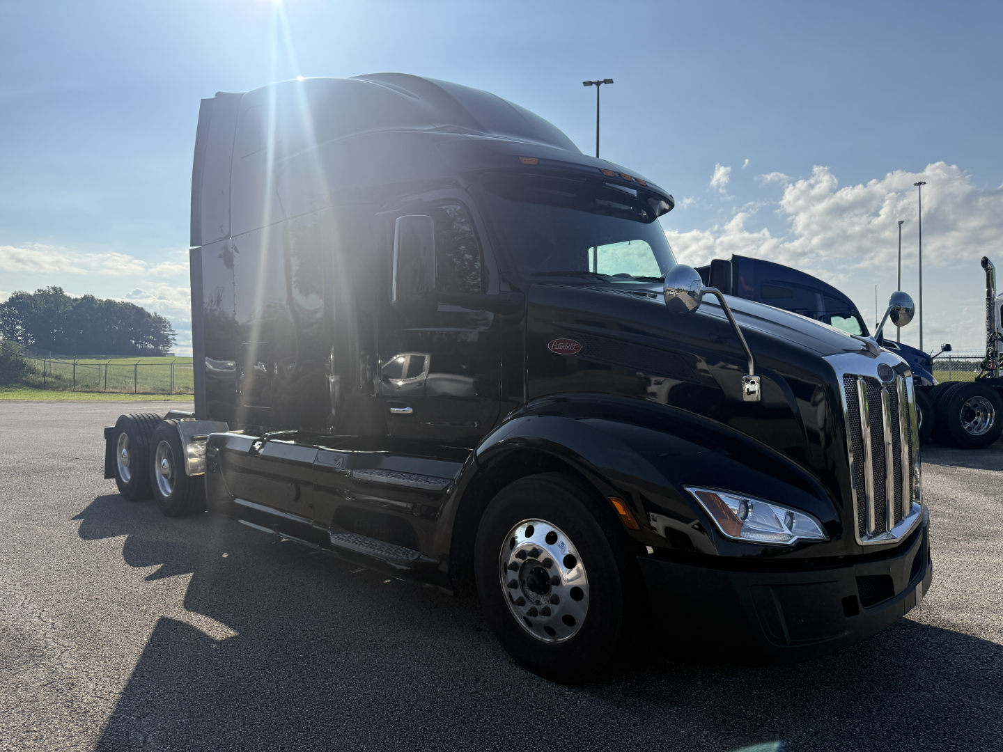 Peterbilt 579 semi-truck cab in black, front-left view, diesel sleeper with chrome wheels and side mirrors, sunlight glare.