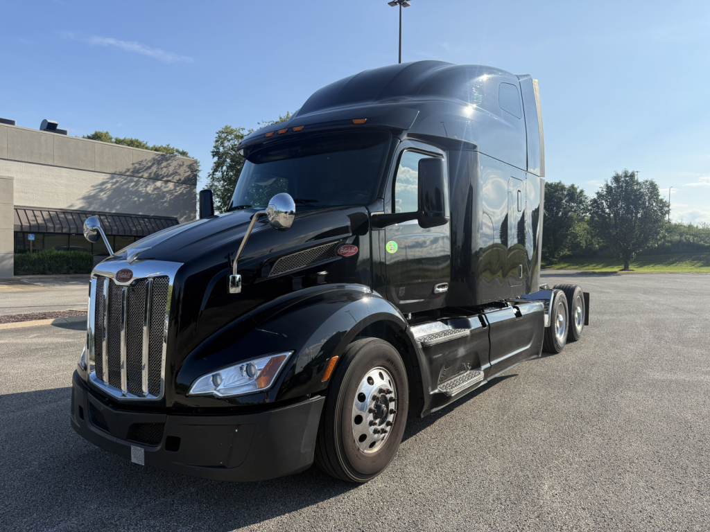 Peterbilt 579 tractor unit in black, front left view showing chrome grille, dual air cleaners, and sleeper cab with windows and side steps.