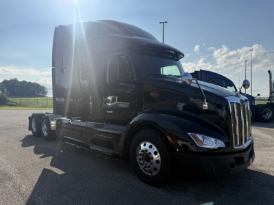 Peterbilt 579 semi-truck cab in black, front-left view, diesel sleeper with chrome wheels and side mirrors, sunlight glare.