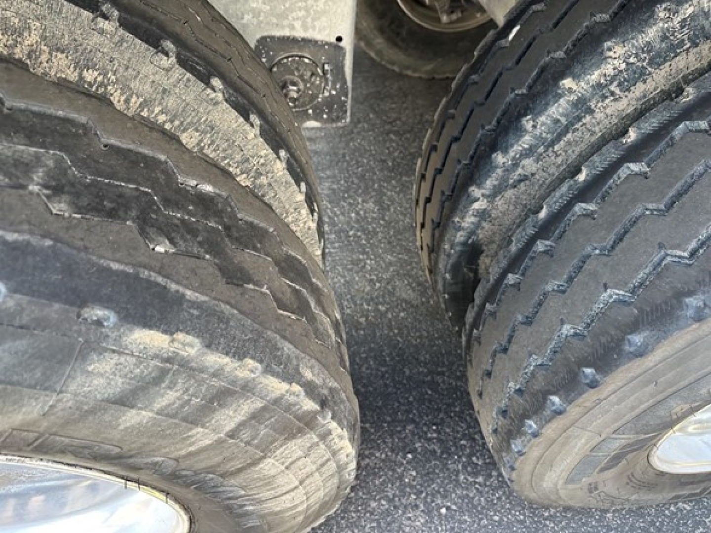 Wheel area of a 2025 Stoughton grain hopper trailer showing dual tires and rough road grime on tread pattern.