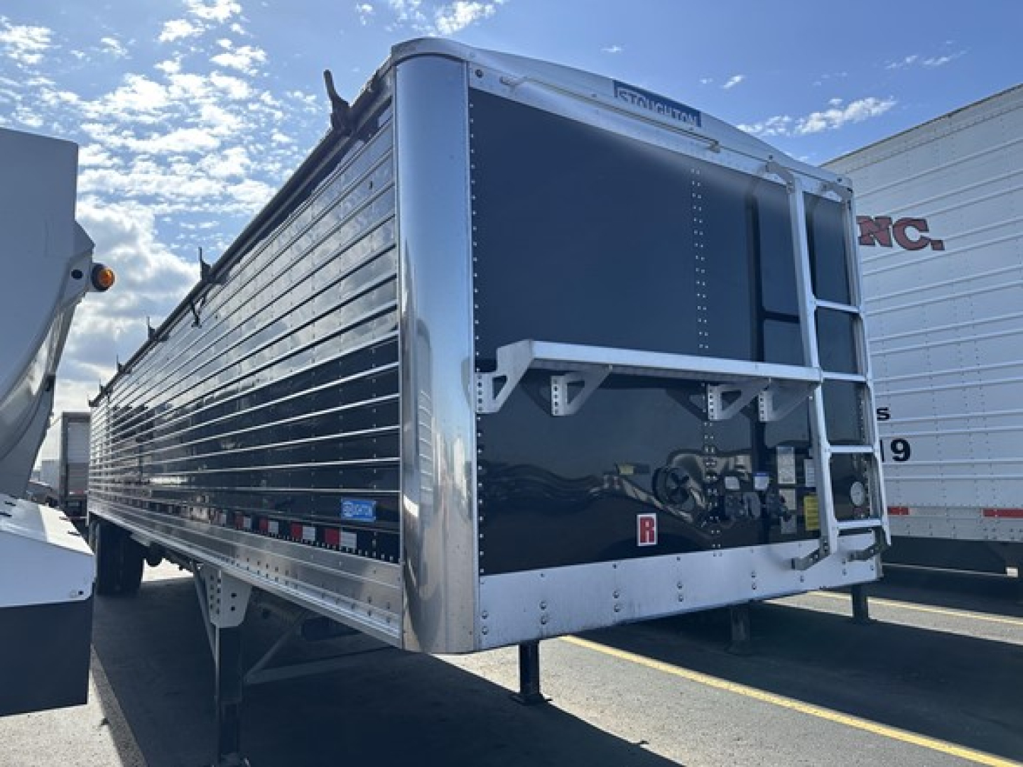 Stoughton grain hopper trailer rear and side view showing aluminum panels and hopper opening, with hydraulic support legs down.