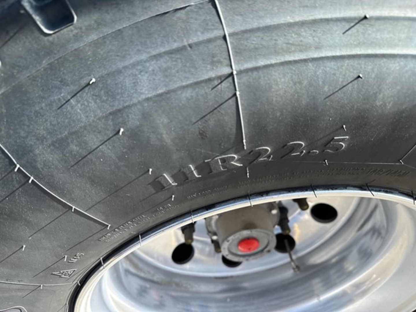 Wheel and tire close-up on 2025 Stoughton grain hopper trailer showing tire tread and wheel with red hub cap.