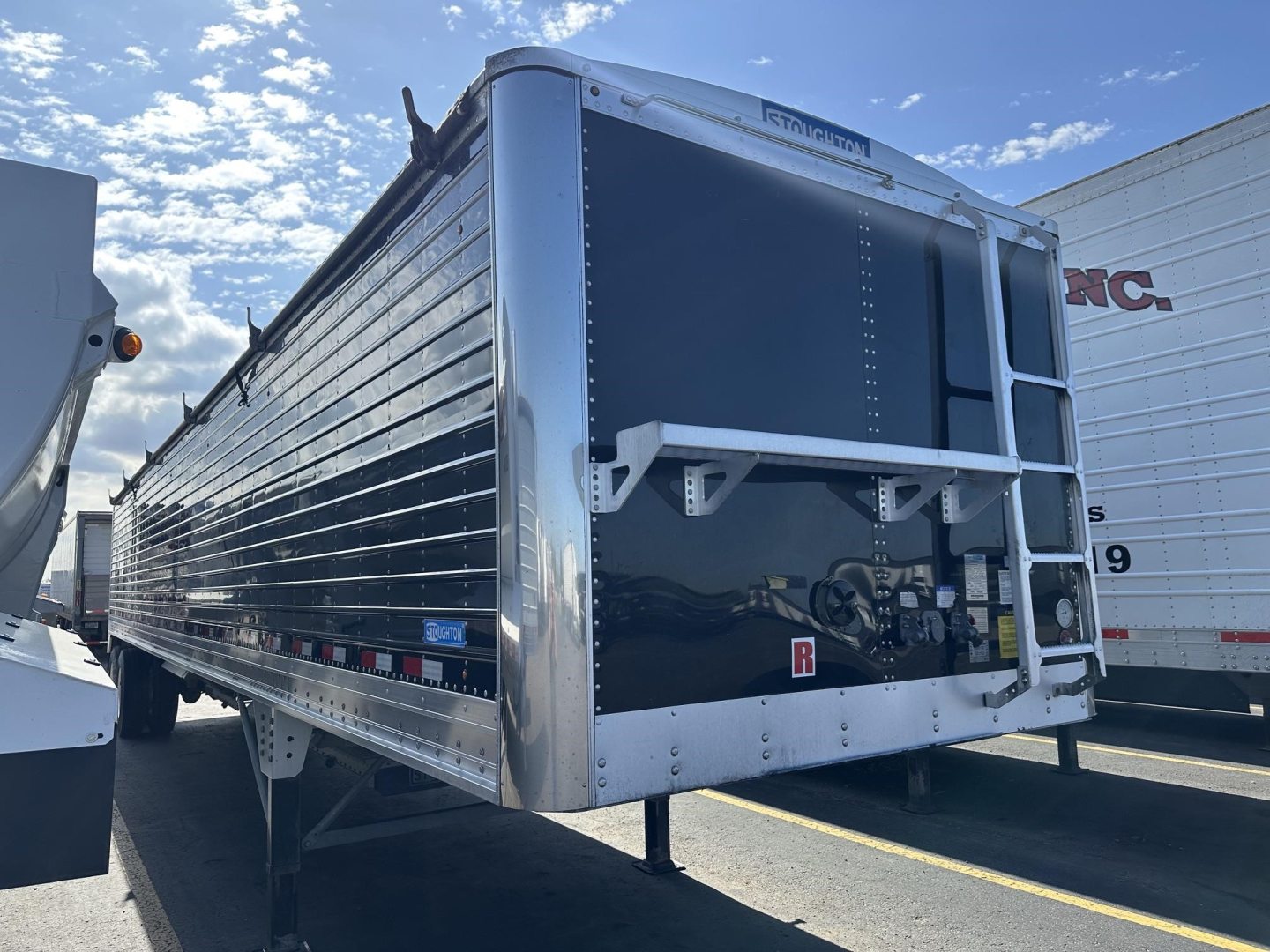 Trailer side view of a dark blue Stoughton hopper trailer with polished aluminum frame, front end with loading door and support legs visible.