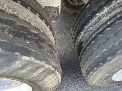 Wheel area of a 2025 Stoughton grain hopper trailer showing dual tires and rough road grime on tread pattern.