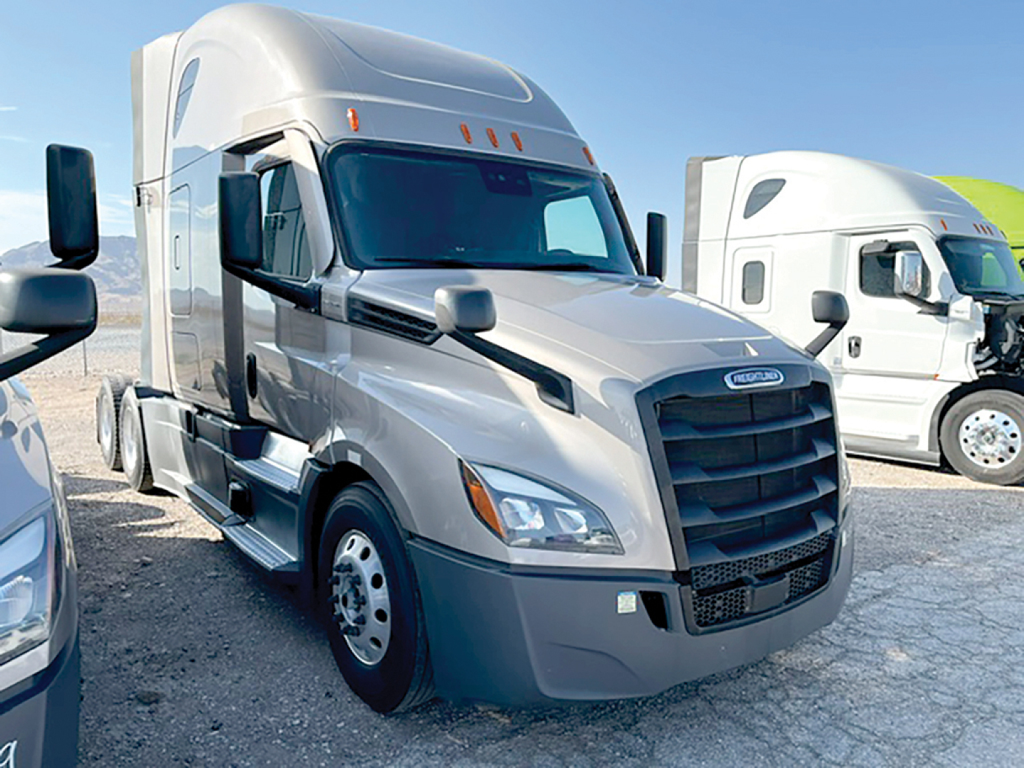 Freightliner Cascadia126 sleeper cab truck in gray with side mirrors, parked lot view, other trucks in background.