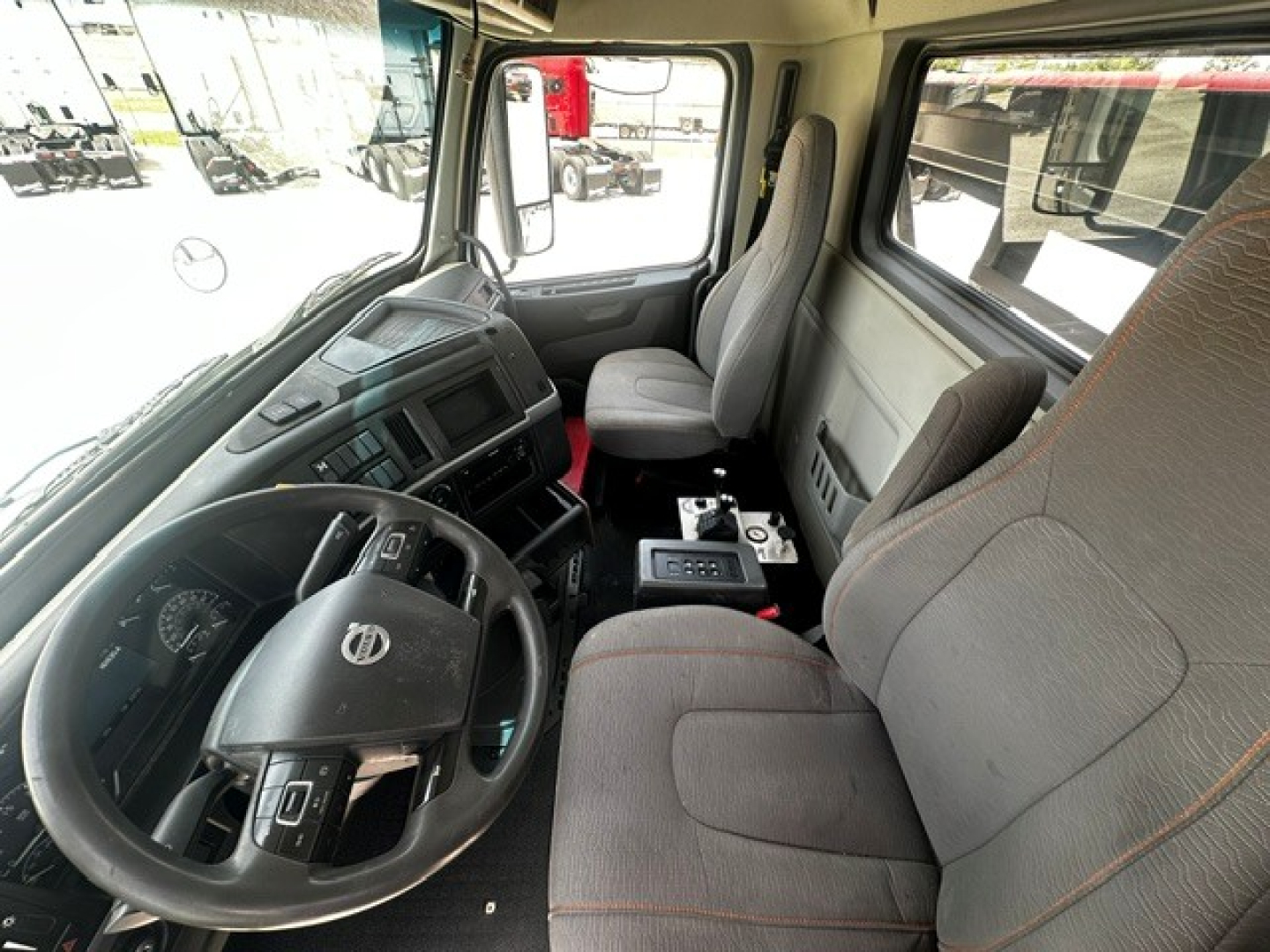Truck cab interior of a 2020 Volvo VHD roll-off truck showing steering wheel, dashboard, driver seat, passenger seat, center console, and gear selector.
