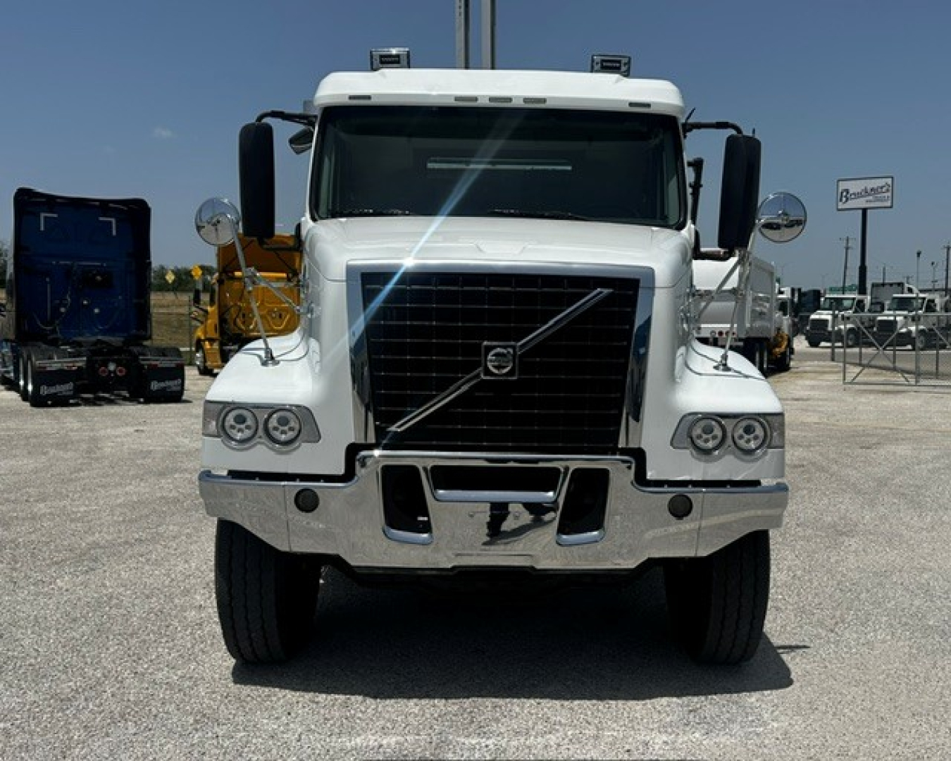 Front view of a white Volvo VHD truck with large grille, bumper, and round side mirrors. No text clearly visible on components.