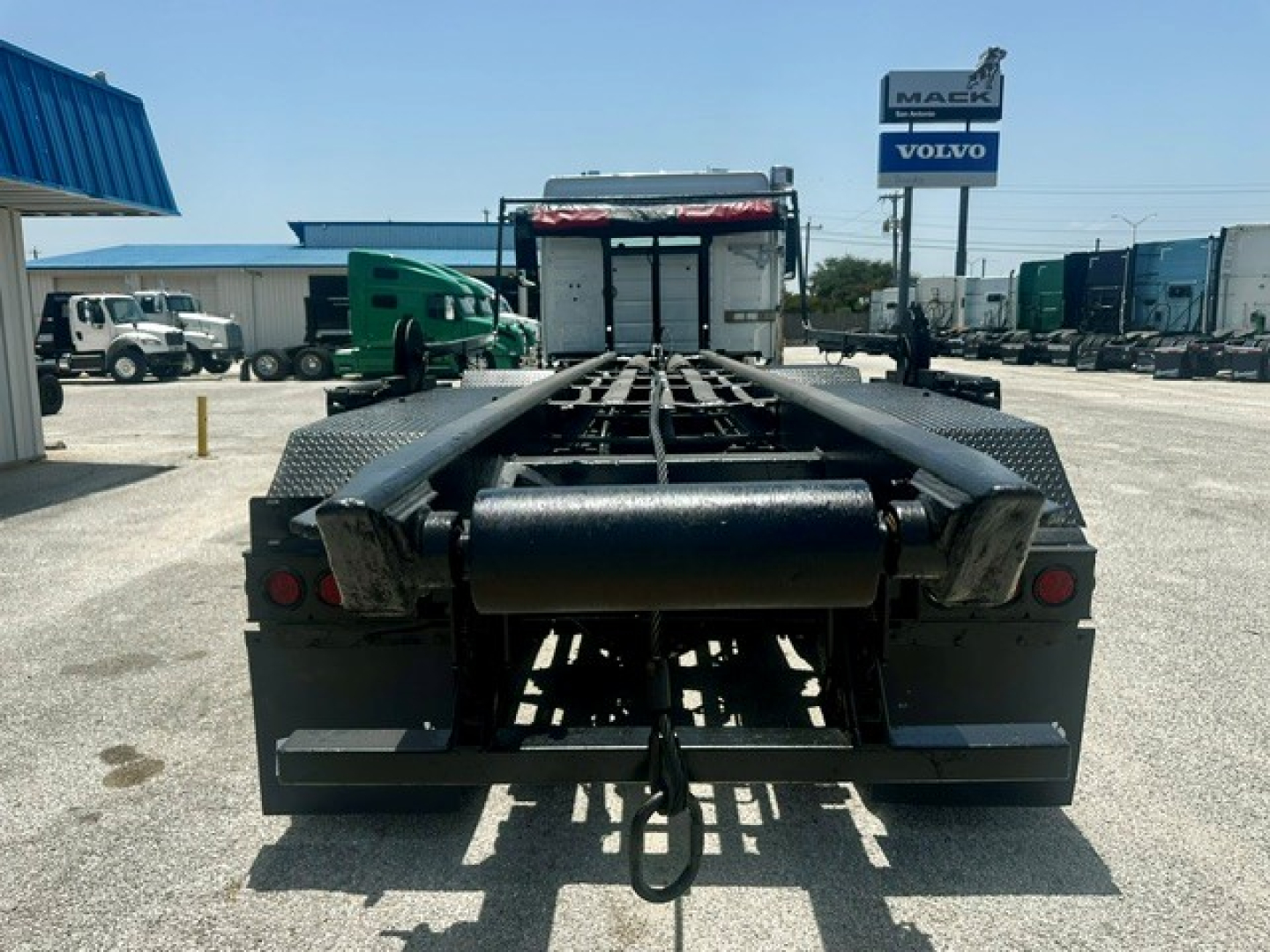 Truck chassis rear view showing gooseneck-style hitch and frame rails, with a Volvo/Mack dealership sign in background.
