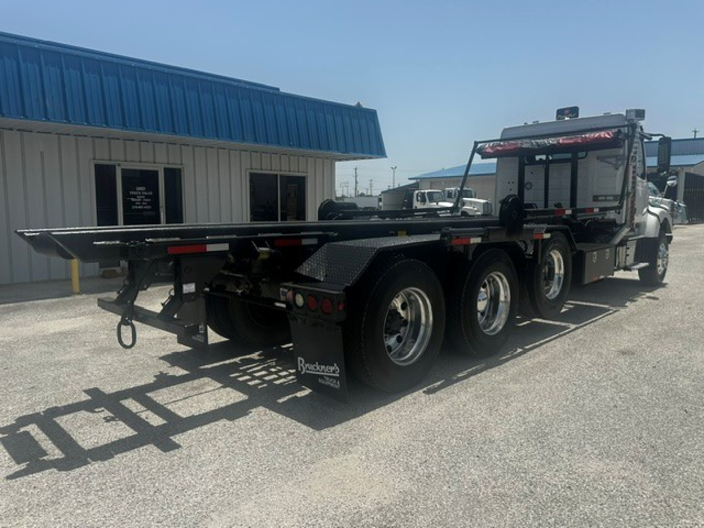 Volvo VHD truck with a flatbed trailer in a lot, side view showing dual rear axles and heavy-duty tires.