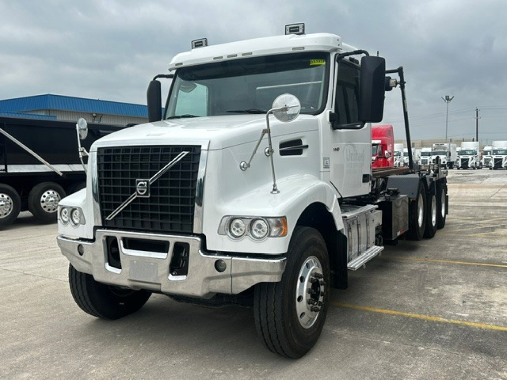 Volvo VHD rolloff truck in white, front-left view with grille, headlights, chrome bumper, and side mirrors.