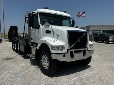 Volvo VHD roll-off truck in white with flatbed and chrome accents, front grille and Volvo emblem visible.