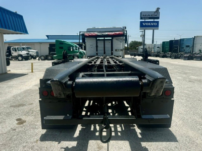 Truck chassis rear view showing gooseneck-style hitch and frame rails, with a Volvo/Mack dealership sign in background.