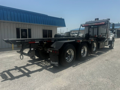 Volvo VHD truck with a flatbed trailer in a lot, side view showing dual rear axles and heavy-duty tires.