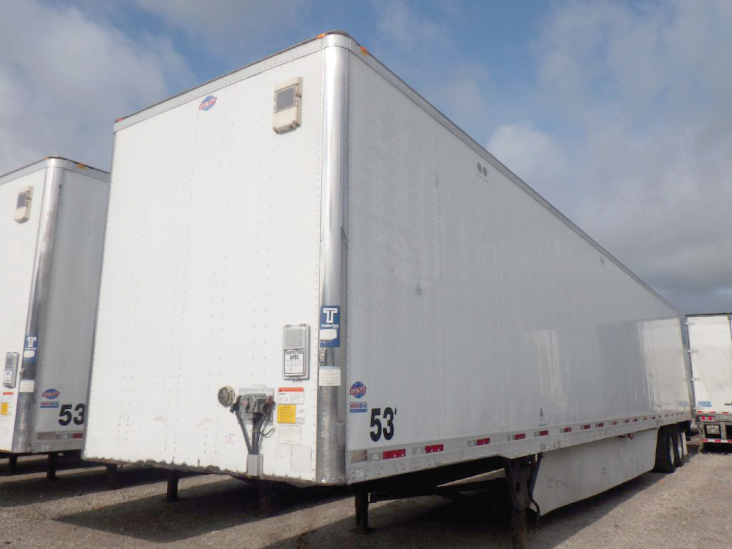 Trailer showing utility 4000D-X yard trailer with rear lights and jack stand, white exterior, side label stickers visible.