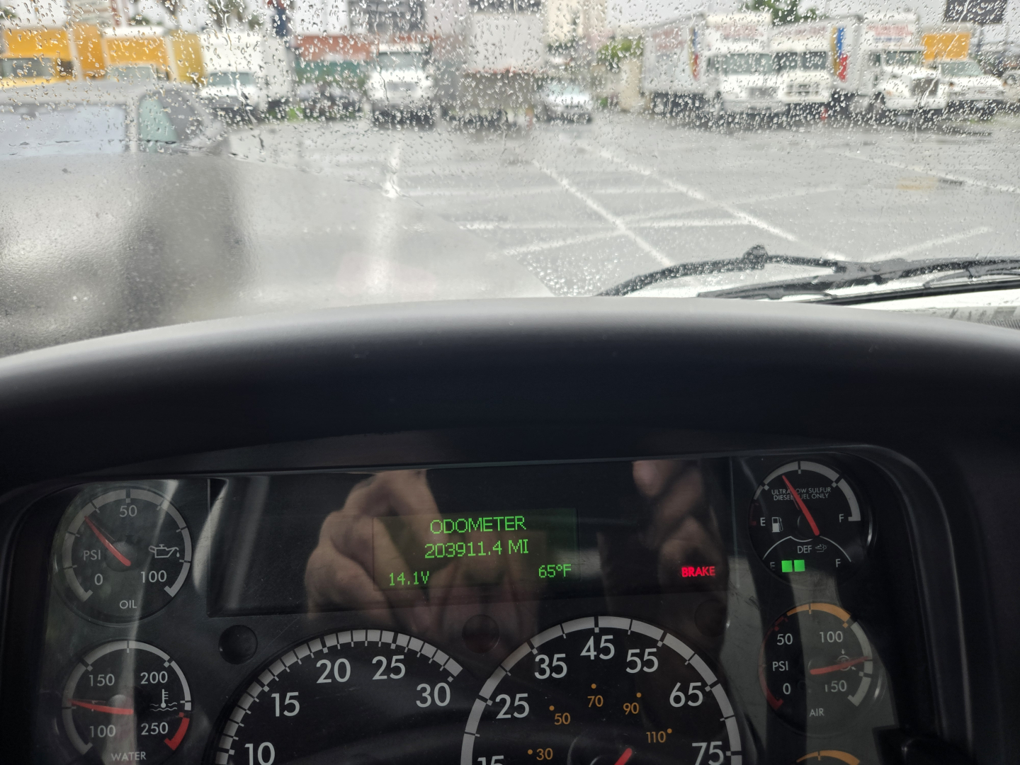 Dashboard view of a Freightliner M2 cab showing digital odometer reading 209,911.4 miles, temperature 65°F, voltage 14.1V, with speedometer and gauges visible.
