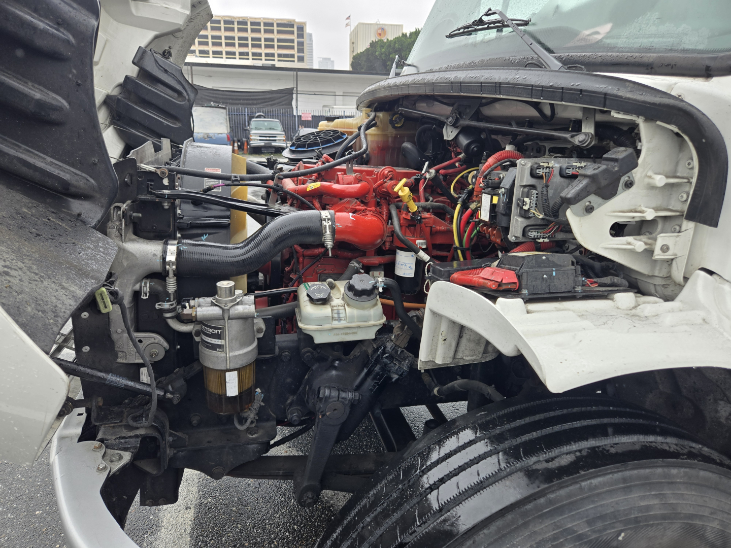 Freightliner M2 engine bay with red-painted engine and various hoses, exposed components, and front wheel visible.