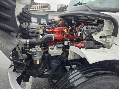 Freightliner M2 engine bay with red-painted engine and various hoses, exposed components, and front wheel visible.