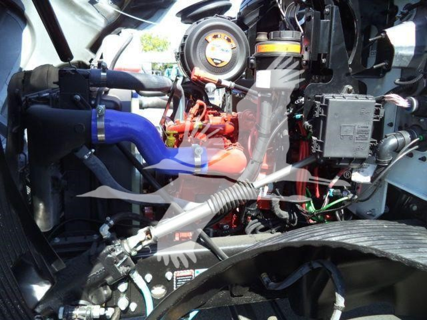 Engine bay of a 2026 Mack MD6 showing blue intake hose, red engine components, wiring, and control modules.