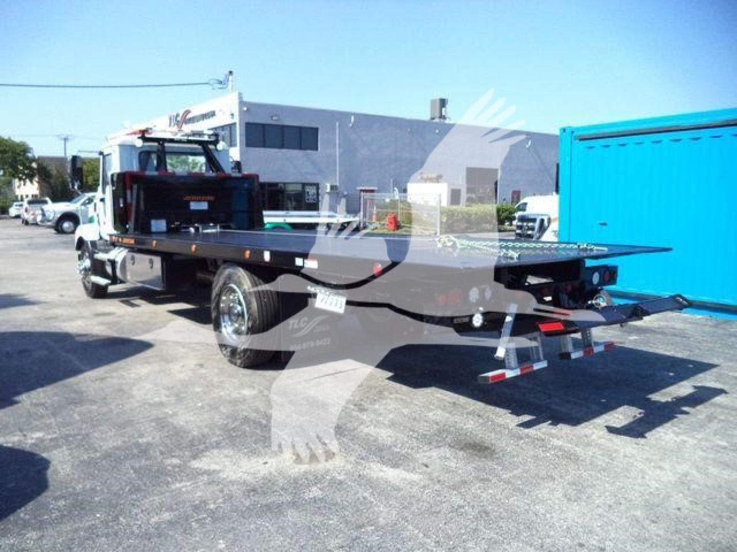 2026 Mack MD6 rollback truck in a yard showing a flatbed bed and rear hitch with blue container in background.
