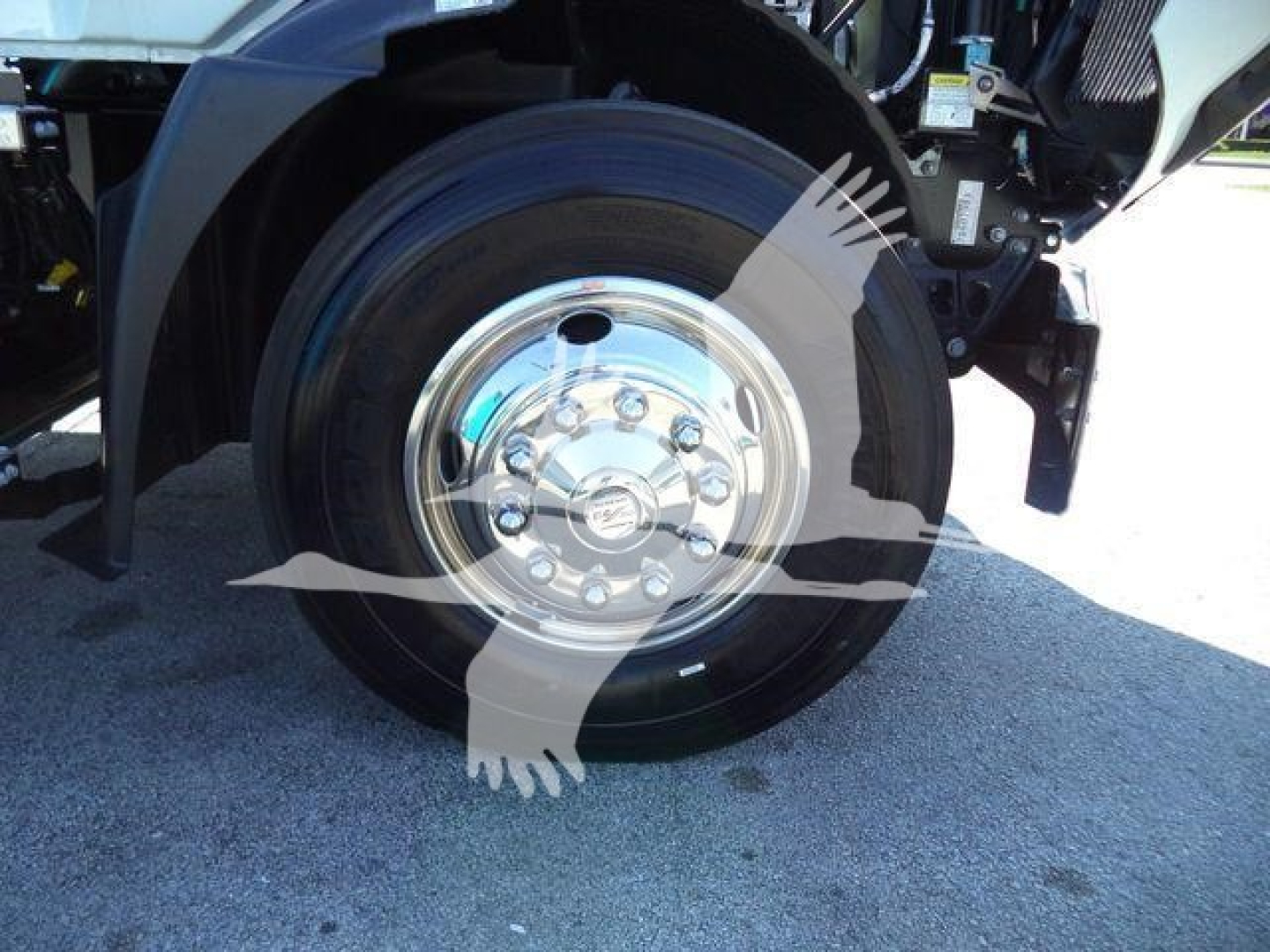 Front wheel and chrome hub of a Mack MD6 truck showing polished steel rim and black tire from a side view.