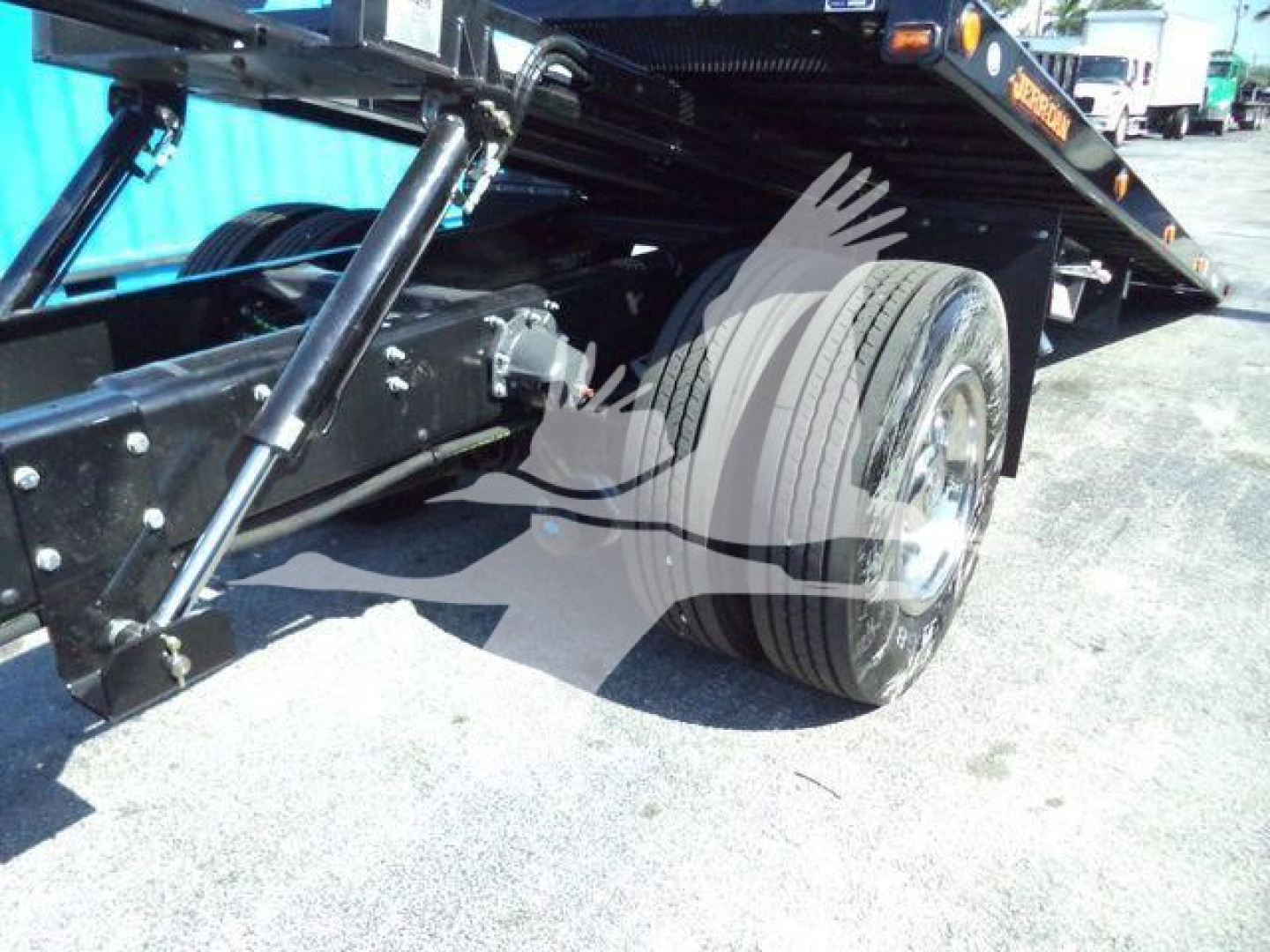 Mack MD6 rear axle and tandem spring suspension under flatbed rollback truck showing wheel and hitch area and hydraulic components.