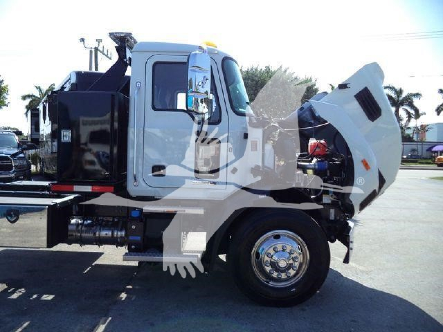 MD6 Mack rollback truck cab with raised front hood, view of engine bay and hydraulic components, white cab, black dump body, front wheel visible.