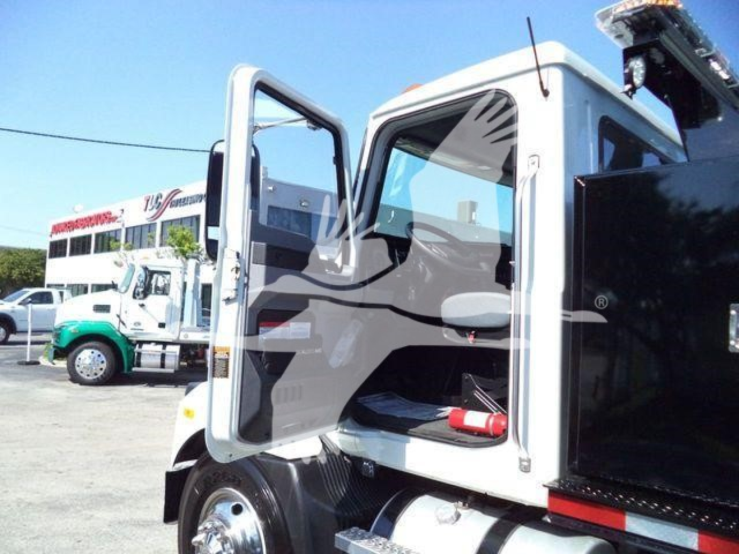 MD6 truck cab open door view showing driver seat and dashboard in foreground; Mack MD6 model truck in a dealership yard.