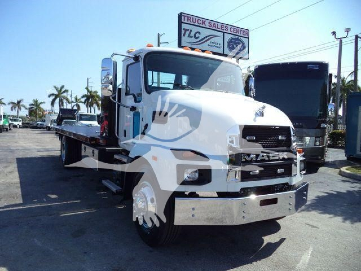 MD6 Mack rollback truck in showroom stance showing front cab and flatbed with chrome bumper and grille, MD6 model emblem not visible, dealership lot in background