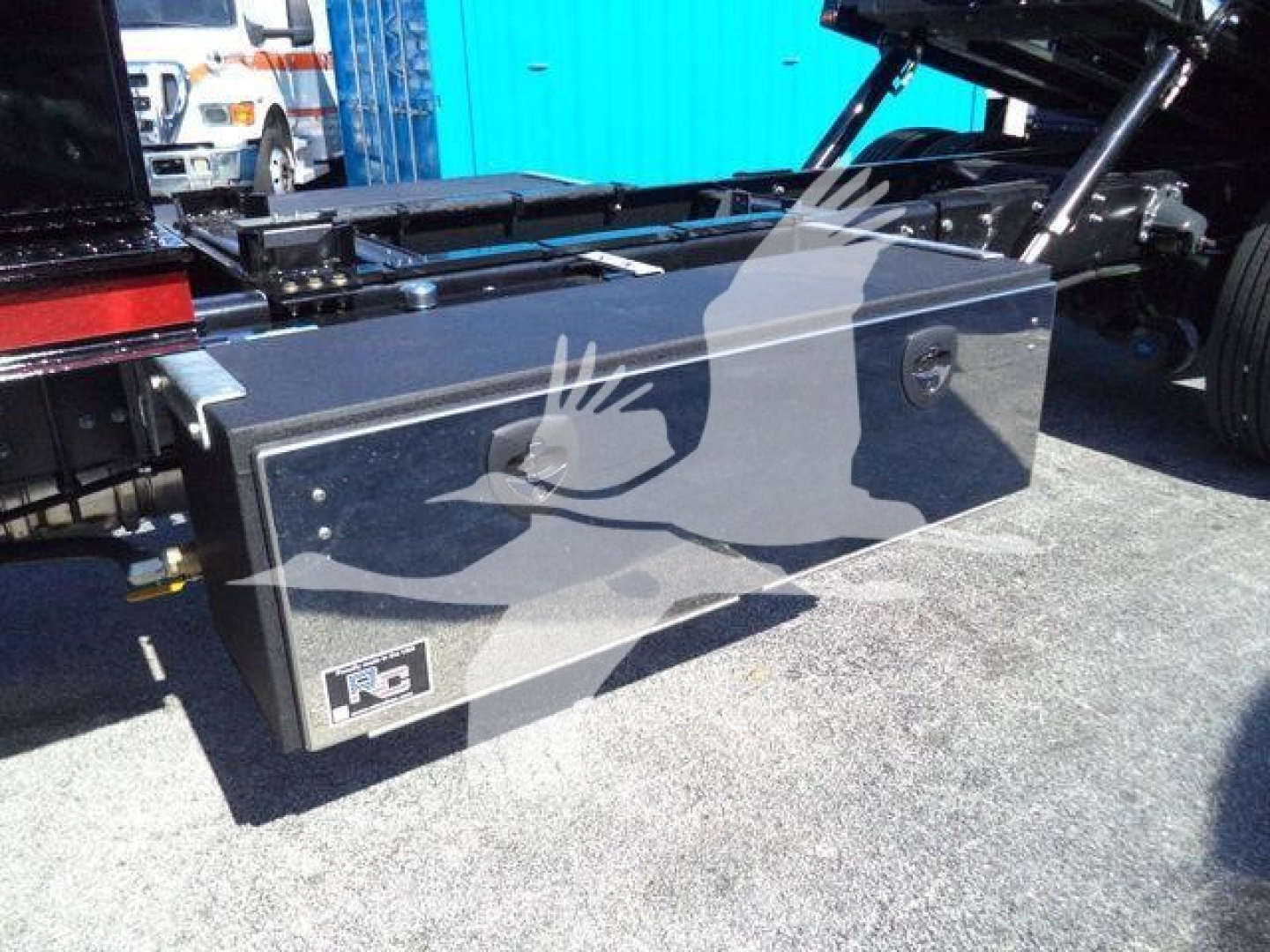 Storage toolbox mounted on a Mack MD6 rollback truck side view showing a rectangular metal tool box with latch and brand label.